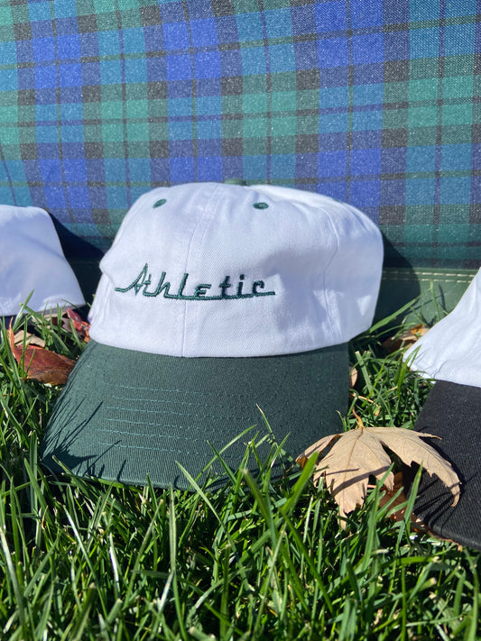 Vintage style white hat with a green brim. Athletic and Affluent calls this colorway "Gas It Green" and the AA club showcases their racing logo in gas it green font as well, reading "Athletic". It sits in front of a vintage plaid luggage in a small pile of fall leaves.