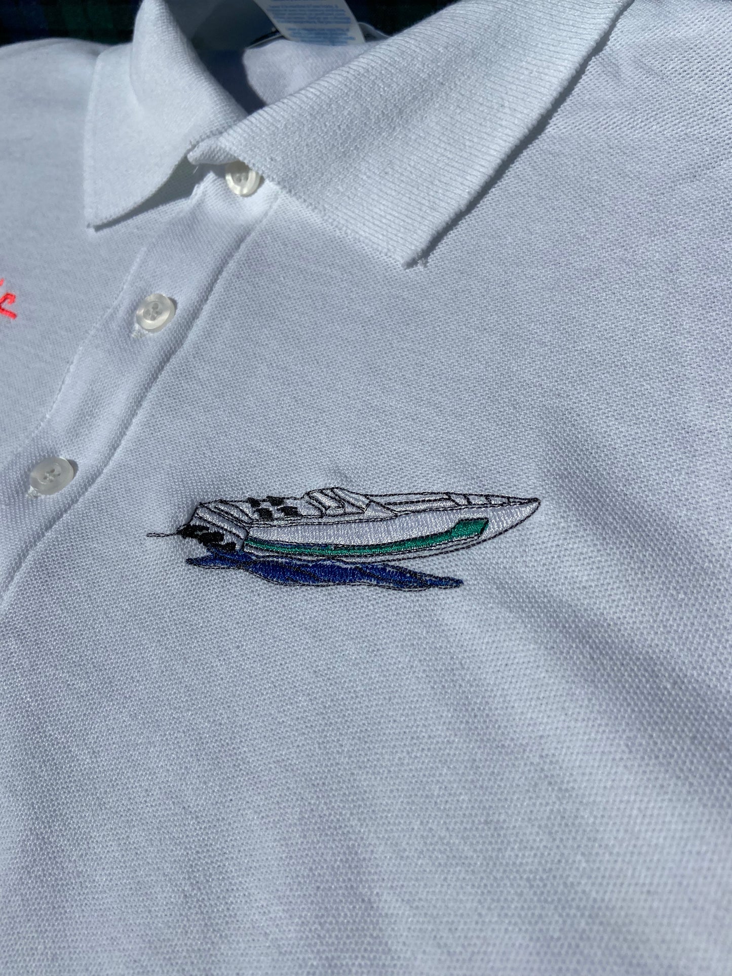 AA Club embroidery on a crisp polo of a white vintage cigarette boat with a teal-green stripe down the side racing through the wavy water.